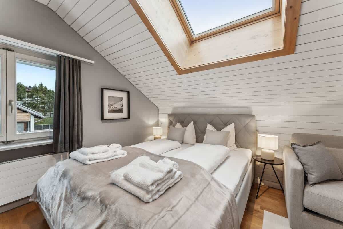 Une chambre avec un puits de lumière, un lit avec des oreillers et une couverture, une table de chevet avec une lampe, et une vue sur l’extérieur.