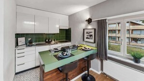 A modern kitchen with a green countertop, white cabinets, and a window with a view of buildings. - book2stay: Retro-Alpin Studio (Laax)