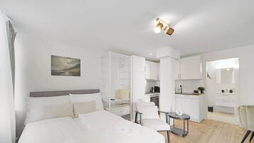 A modern hotel room with a large bed, a small desk, and a kitchenette.