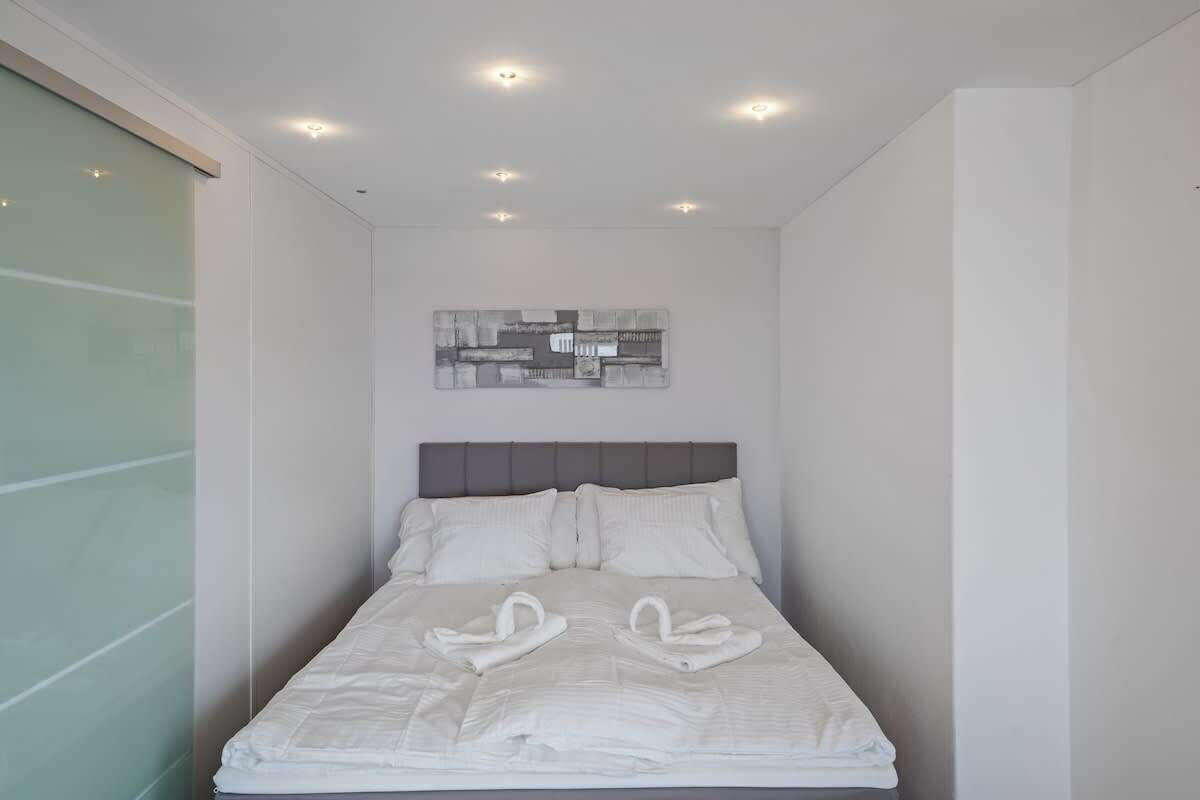 A modern hotel room with a neatly made bed, a gray headboard, and a wall-mounted abstract art piece.
