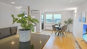 A modern living room with a dining area, large windows, and a view of the city. - book2stay: Lakefront Apt w/Balcony, near Harbor & Station (Romanshorn)