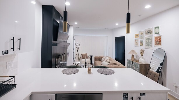 A modern kitchen with a white countertop, black cabinets, and pendant lighting.