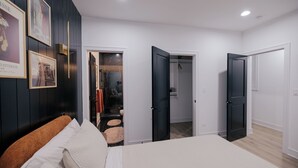 A modern bedroom with a large bed, a wardrobe, and a bathroom visible through an open door.