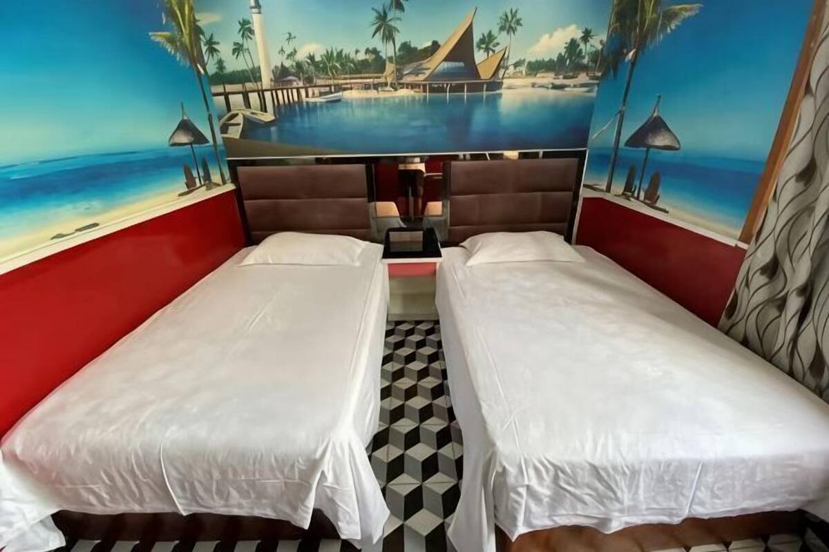 A room with two beds, a checkered floor, and a mural of a beach scene.