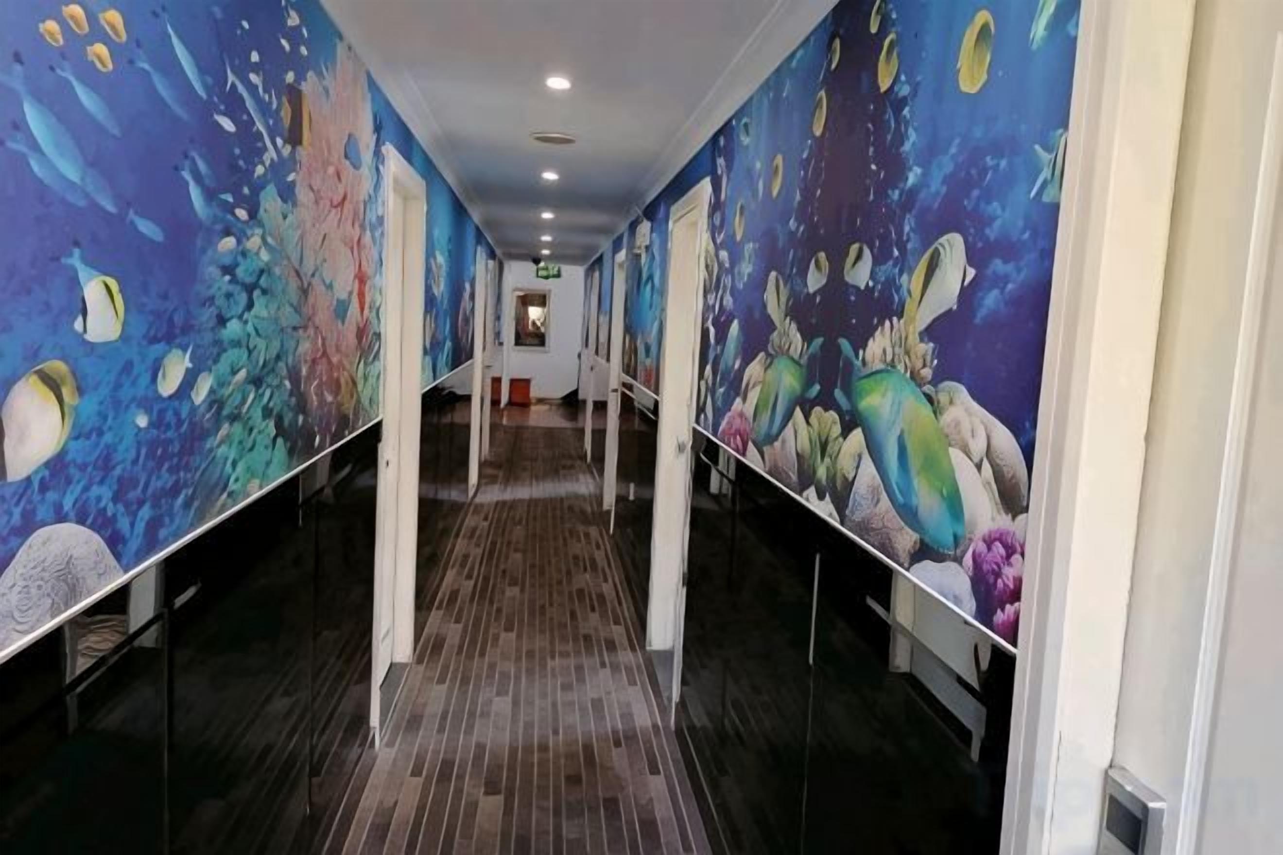 A hallway with a long corridor, walls adorned with colorful murals, and a wooden floor.
