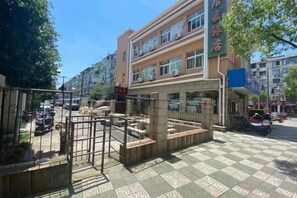 Entrada de hotel com uma entrada por portão, calçada de azulejos e um edifício de vários andares com letreiros.