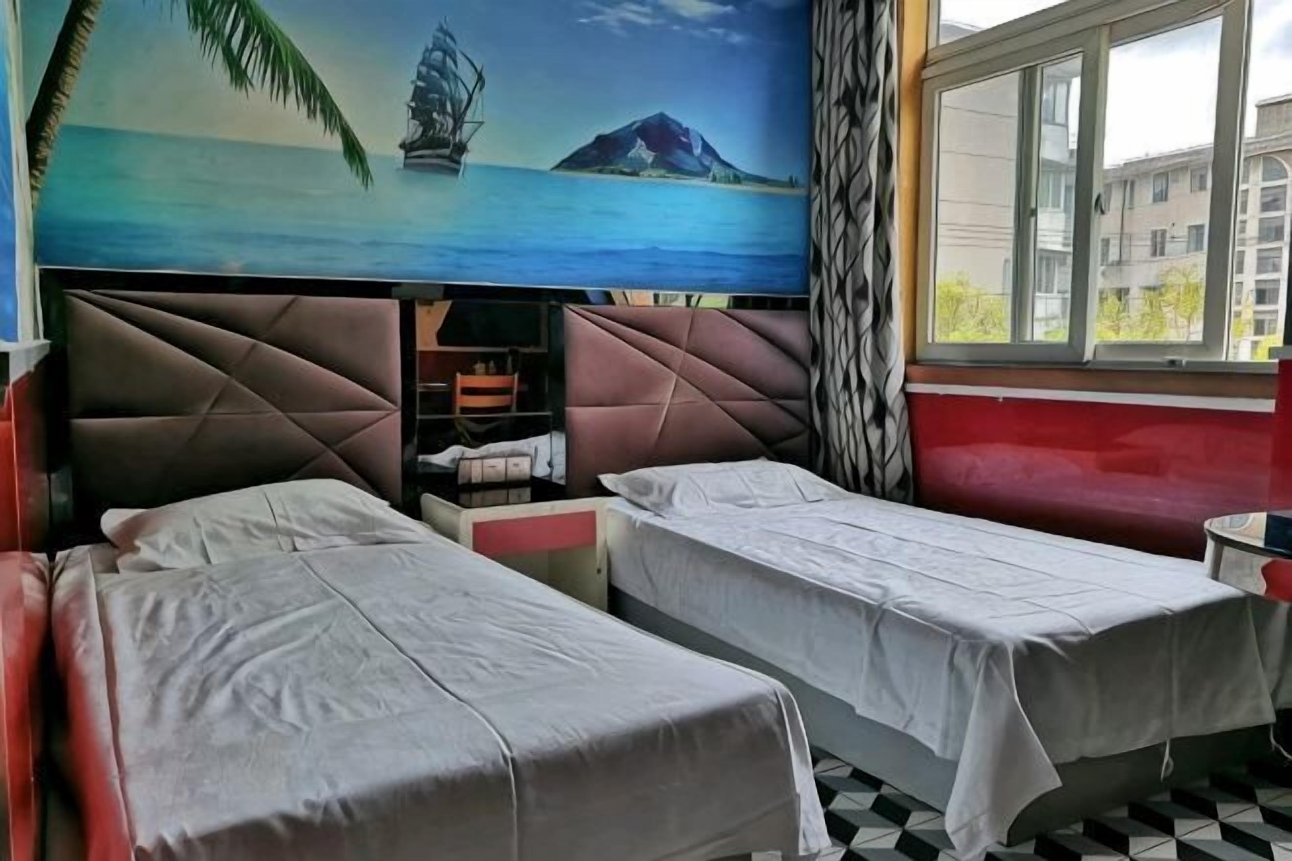 A room with two beds, a window with a view, a wall with a mural, and a patterned floor.