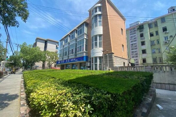 A multi-story building with a blue storefront, surrounded by greenery and adjacent to other buildings. - Jujia Hostel (Shanghai)