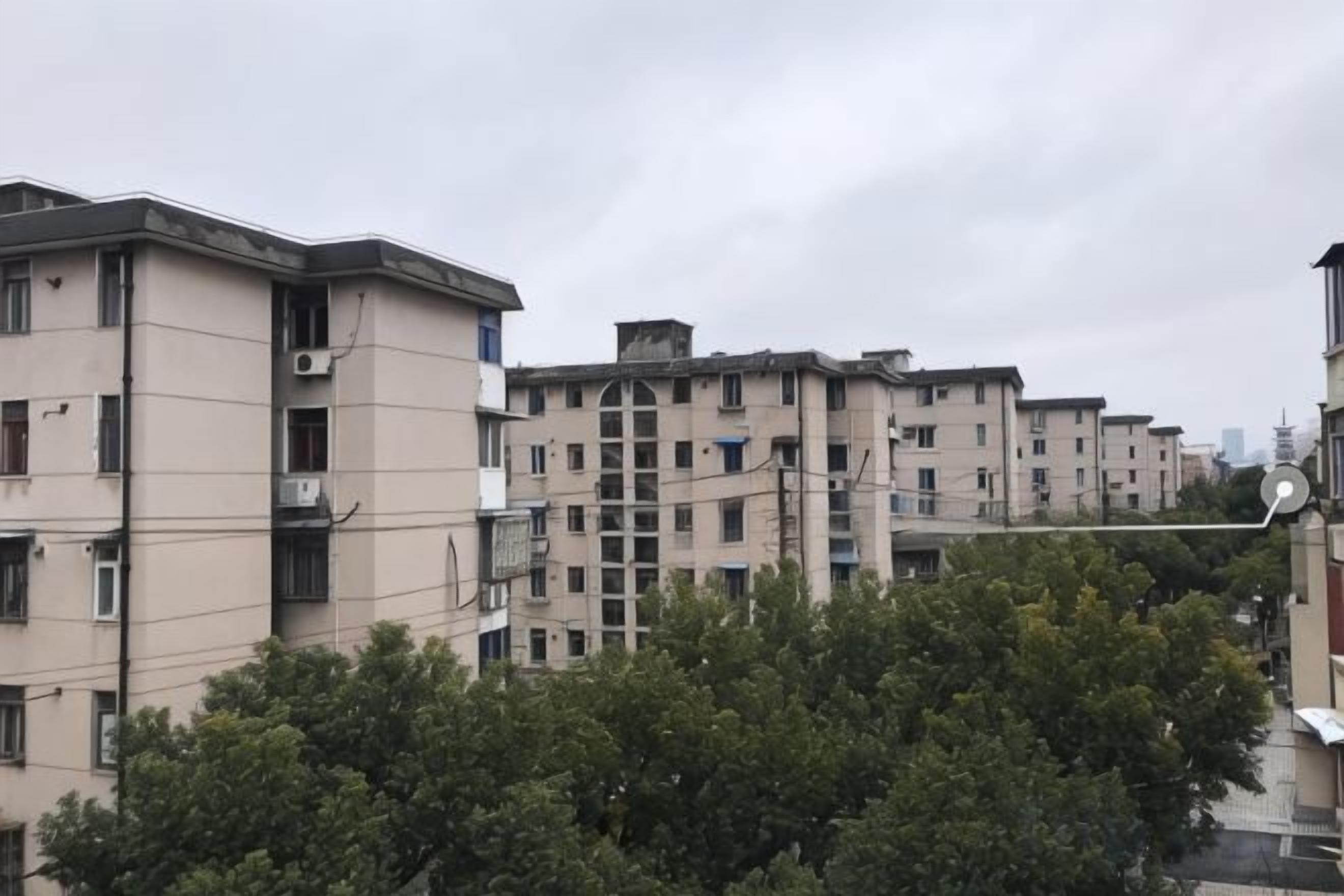 A row of multi-story residential buildings with balconies, surrounded by trees.