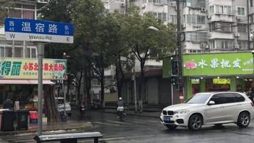 Vista d'un carrer amb un senyal de Wensu Rd, una botiga de fruita i un SUV blanc.