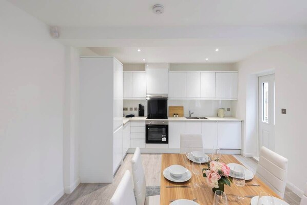 A modern kitchen with white cabinets, a dining table set for four, and a built-in oven.