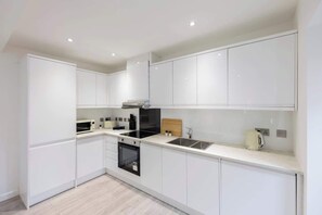 A modern kitchen with white cabinetry, a black stove, a microwave, and a kettle.