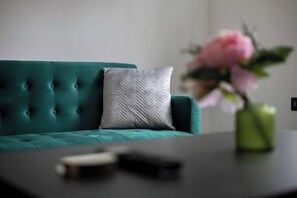 Un canapé de couleur turquoise avec un coussin texturé, une télécommande et un vase rempli de fleurs posé sur une table.