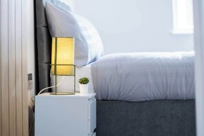 A bedroom with a bed, bedside table, lamp, and a small plant.