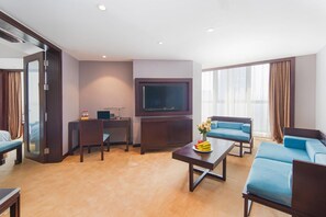 A hotel room with a flat-screen TV mounted on the wall, a desk with a chair, a sofa, and a coffee table with fruit. - Vienna International Hotel (Suzhou)
