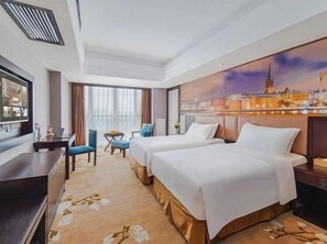 A hotel room with two beds, a desk, a chair, a TV, and a cityscape painting on the wall. - Vienna International Hotel (Suzhou)