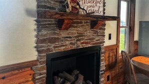 A stone fireplace with a sign above it, a wooden dining table, and a view of the outdoors through a window.