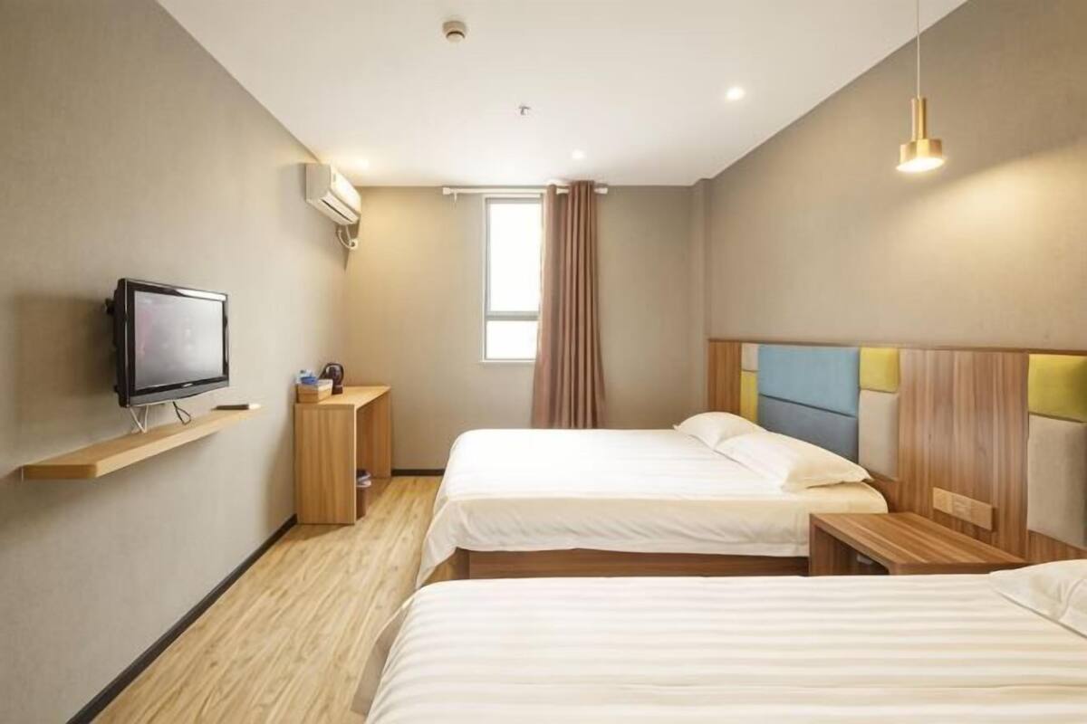 A hotel room with two beds, a TV, a small table, and a window with curtains.
