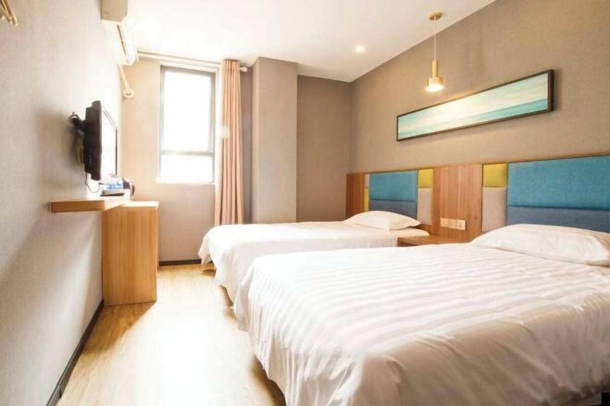 A hotel room with two beds, a television, a window with curtains, and a painting on the wall.
