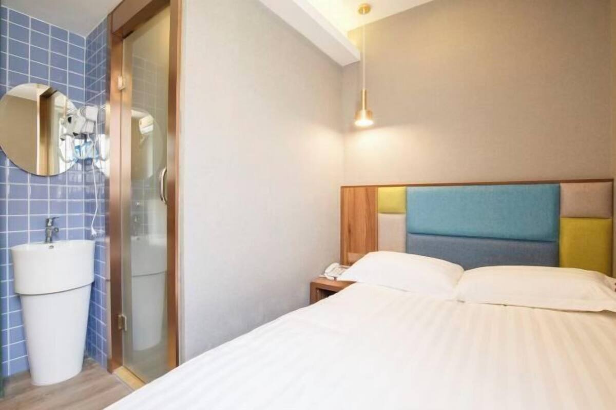 A hotel room with a bed, a bedside table with a phone, a mirror, and a sink.