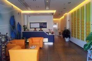 Zona de recepció d'hotel amb una taula de recepció, dos sofàs i un mural gran a la paret.
