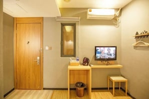 A small room with a wooden door, a mirror, a television, a small table, a trash bin, and a shelf with decorative items. - Ripple Yun Hotel (Shanghai Xinqiao Xinjia Plaza) (Shanghai)