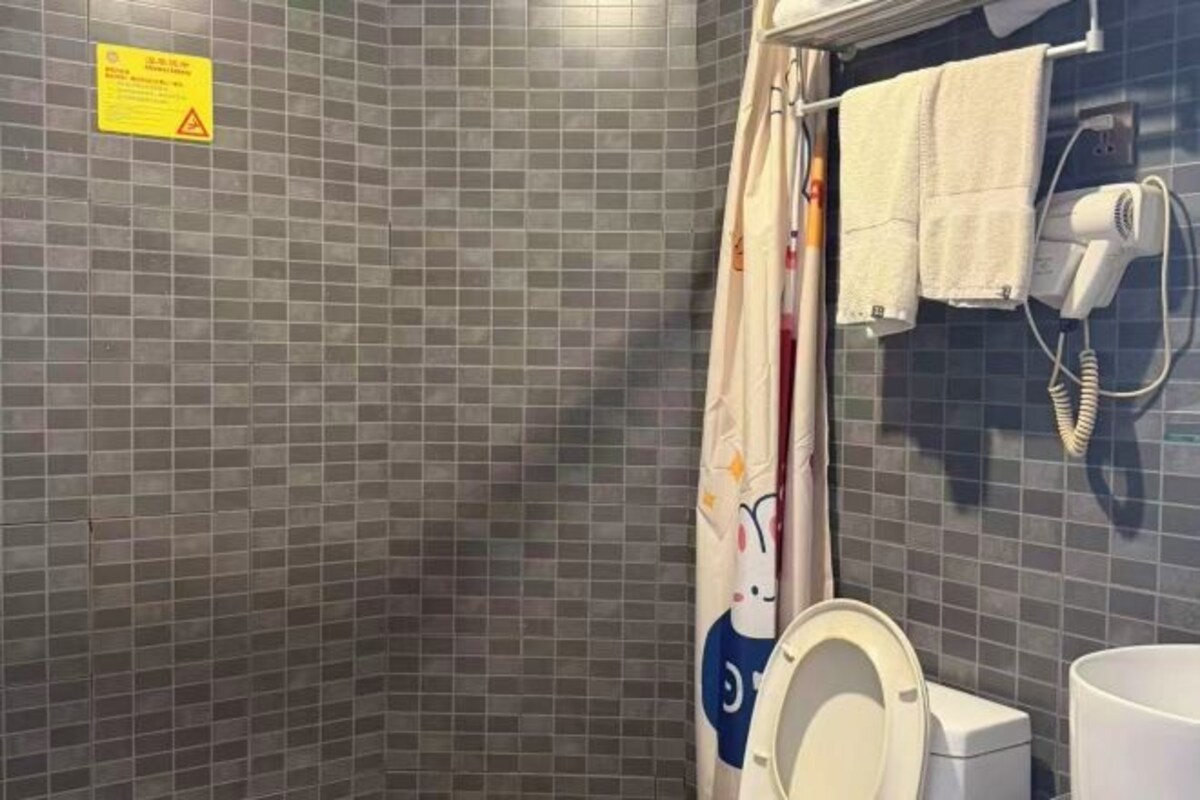 A bathroom with a tiled wall, a toilet, a shower curtain, and a hairdryer on the wall.