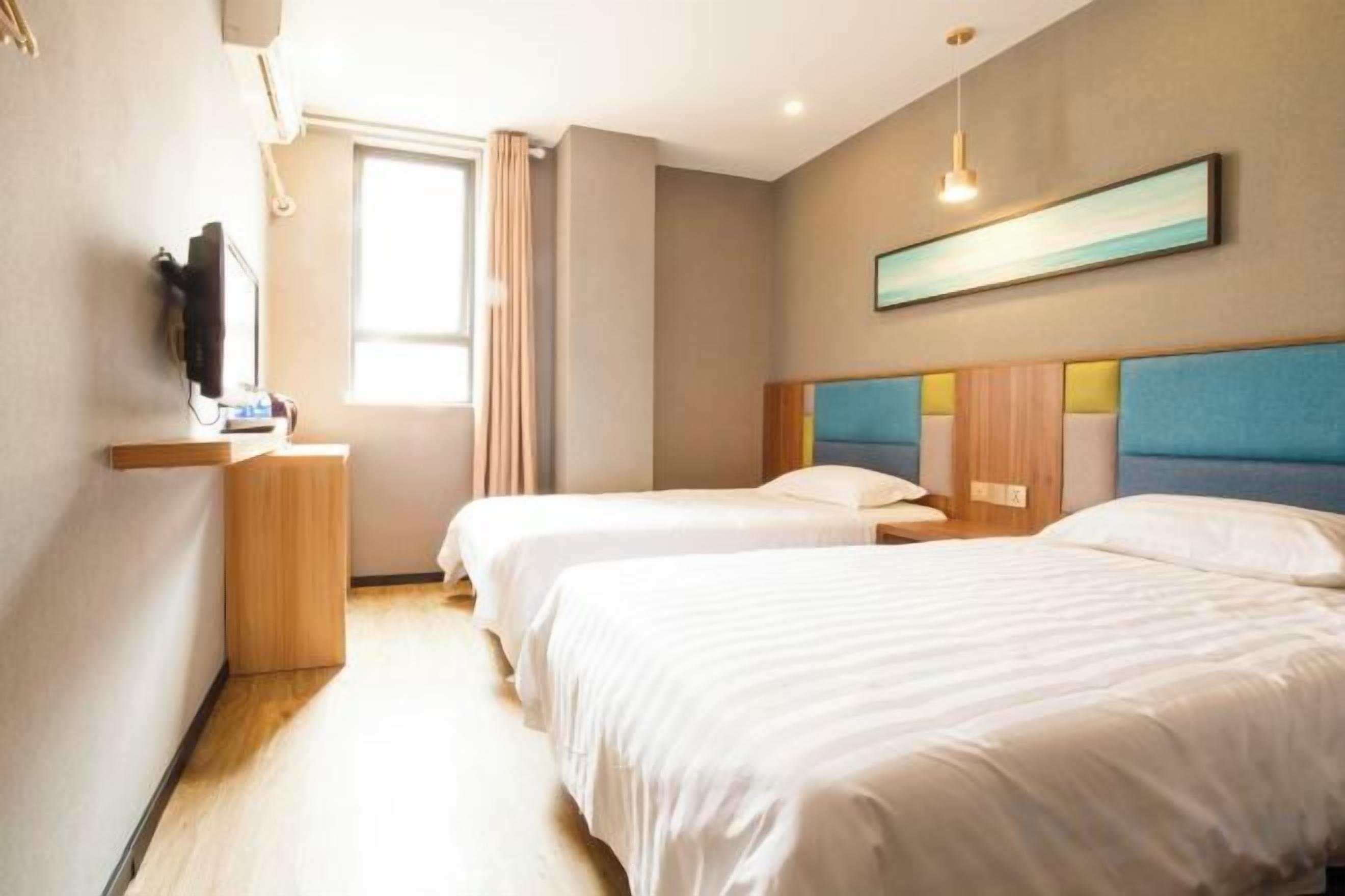 A hotel room with two beds, a TV, a desk, and a window with curtains.