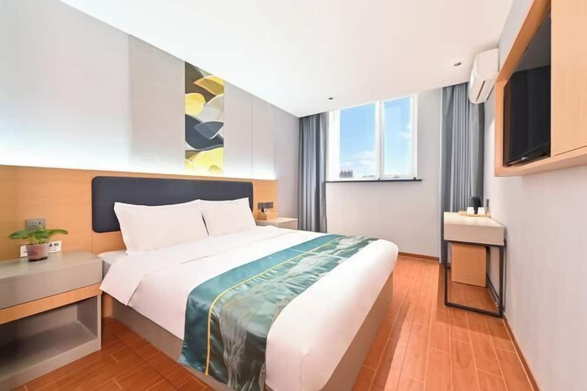 A hotel room with a bed, bedside table, a wall-mounted TV, a window, and a bathroom with a sink and mirror.