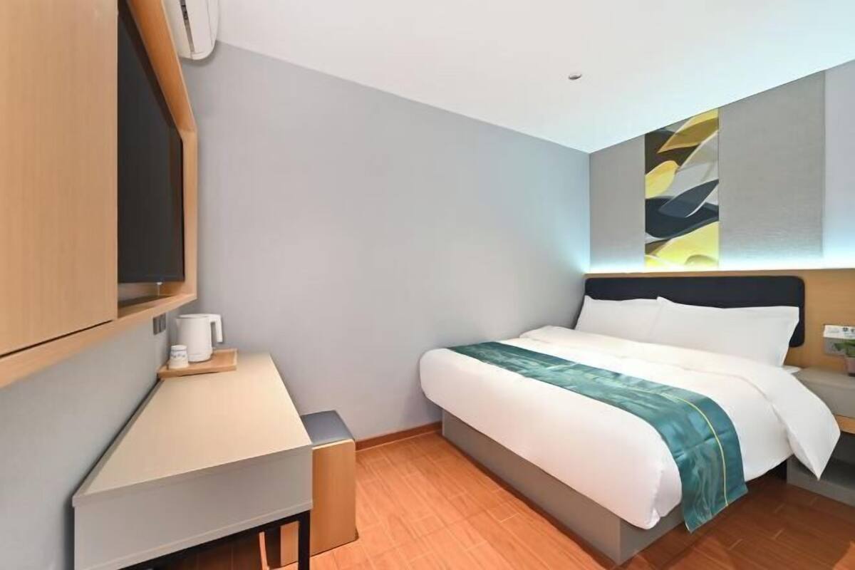 A modern hotel room with a bed, a desk, a chair, and a TV.