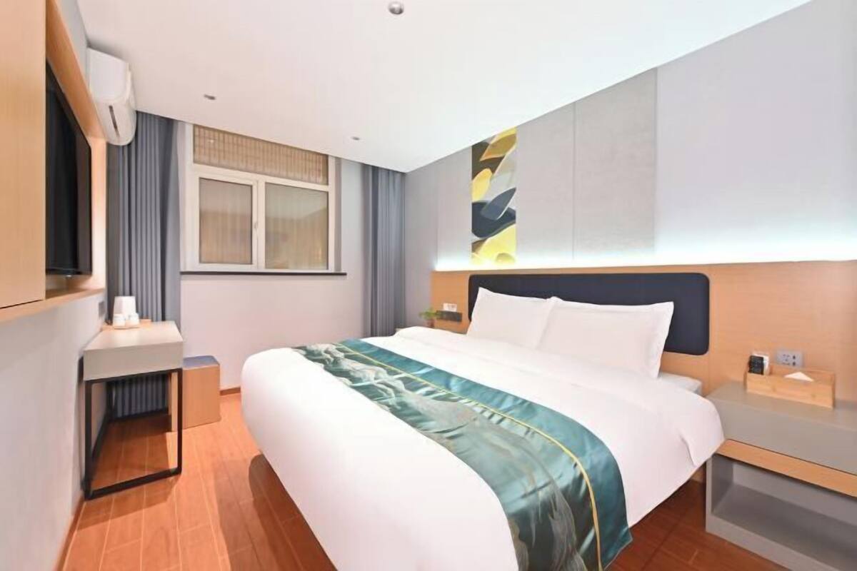 A hotel room with a bed, bedside table, nightstand, and a window with curtains.