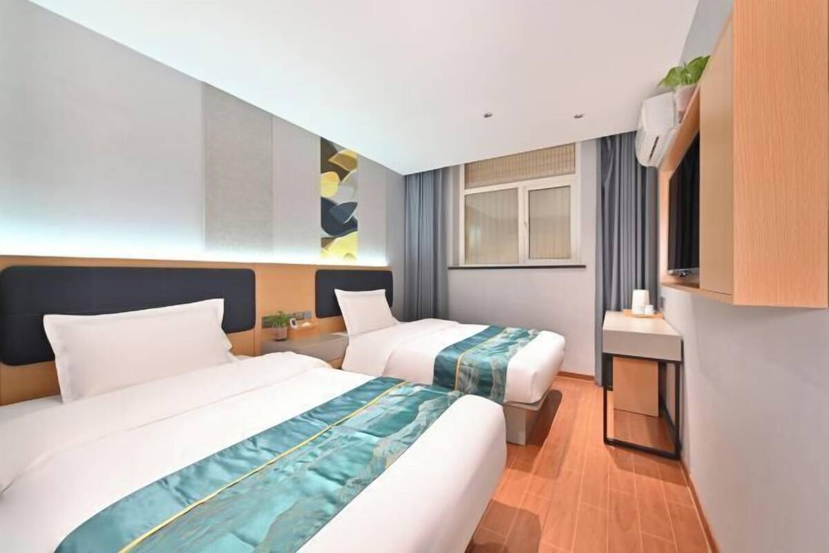 A hotel room with two beds, a small desk, a TV, and a window with curtains.