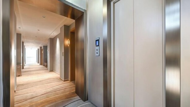 A modern hotel corridor with a wooden floor, a metallic elevator, and a control panel on the wall. - Youyue Selected Hotel (Beijing South Station Temple of Heaven South Gate Branch) (Beijing)