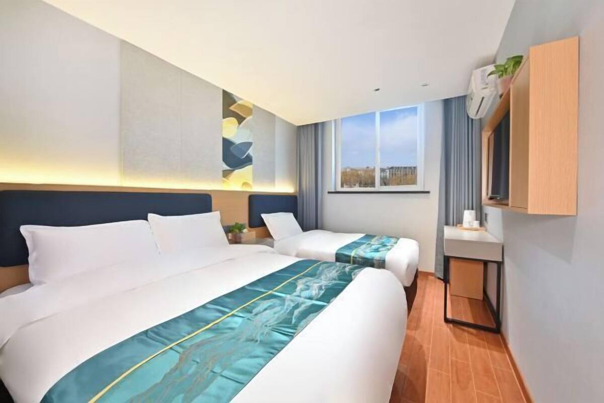 A hotel room with two beds, a small bedside table, a wall-mounted TV, and a window with a view.