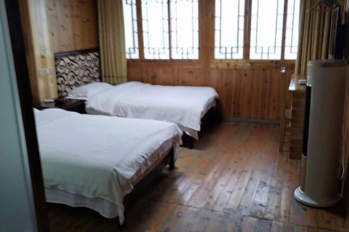 A room with two beds, wooden walls, and a window with bars.