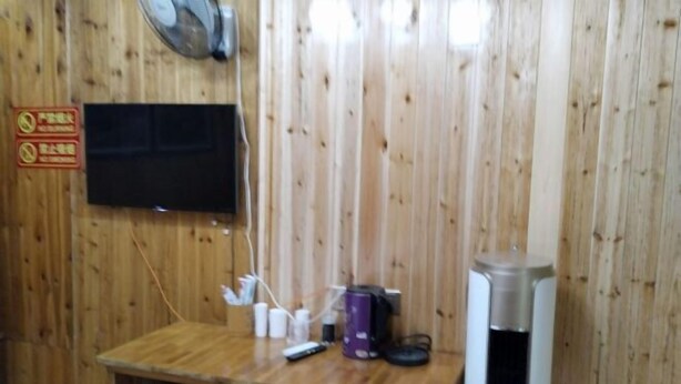 A wooden wall with a mounted television, a small table with various items, and a trash can. - Chiyou Valley Homestay (Xinhua)