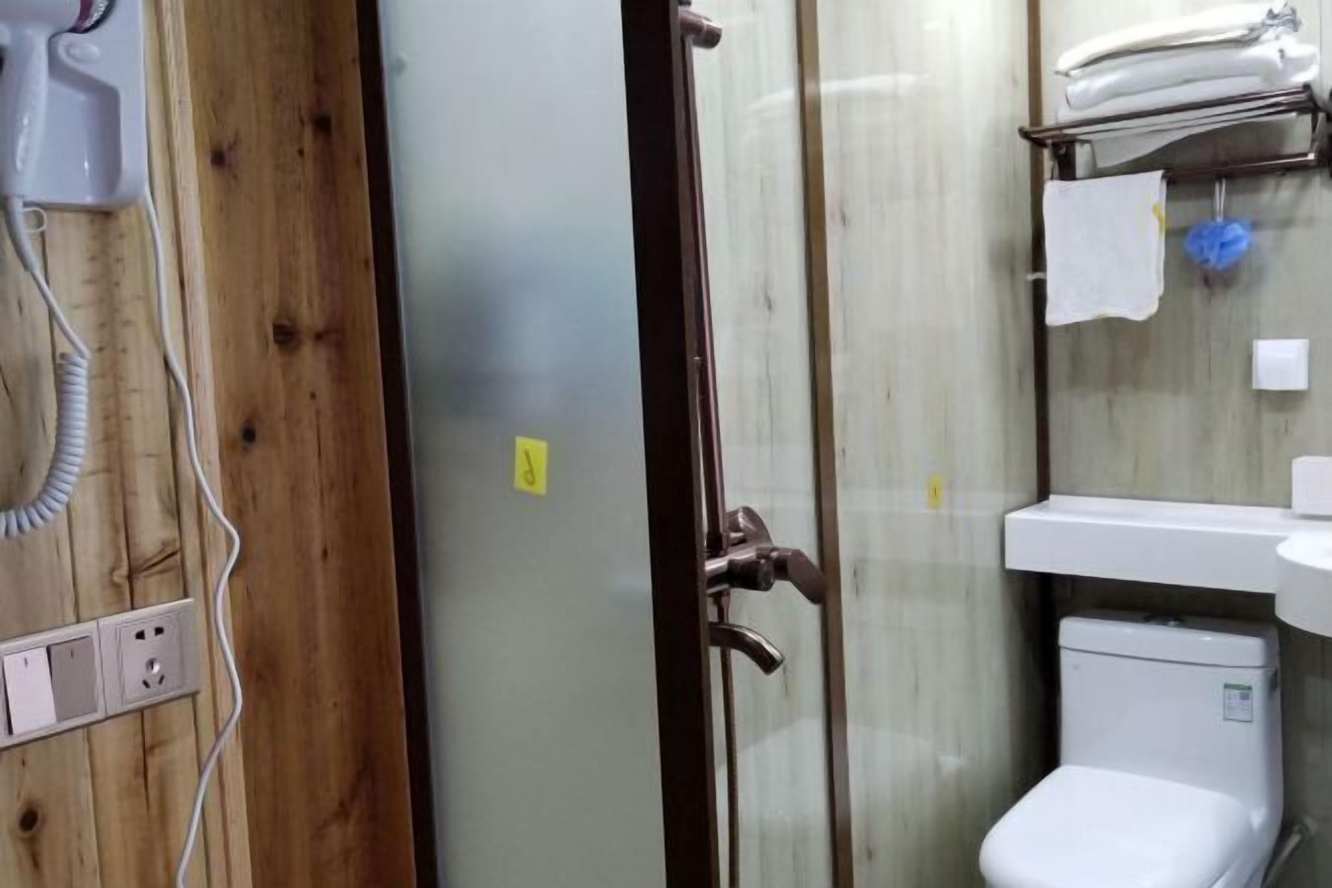 A bathroom with a wooden panel wall, a glass shower enclosure, a white toilet, and a sink with a towel rack.