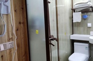 Uma casa de banho com parede revestida a madeira, cabine de duche em vidro, sanita branca e lavatório com um porta-toalhas.
