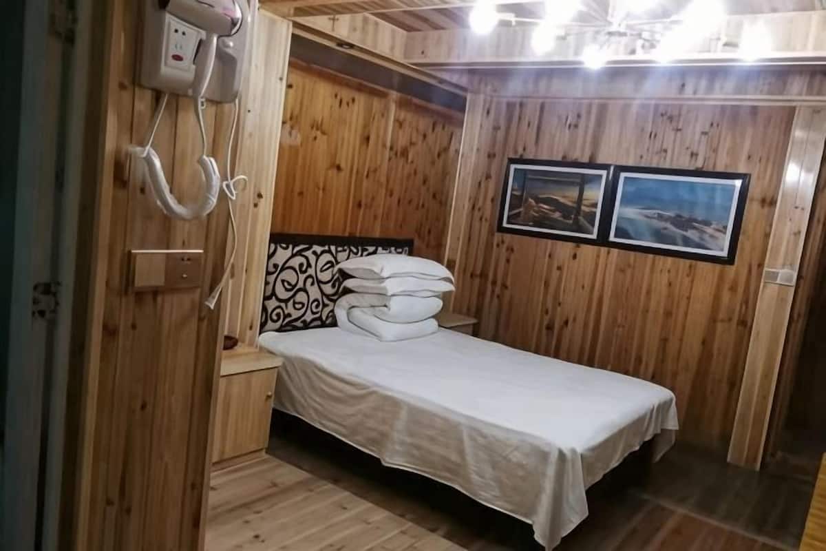 A wooden-paneled room with a bed, a bedside telephone, and two framed pictures on the wall.