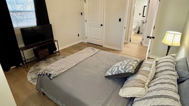 A bedroom with a bed, a ceiling fan, a TV, and a bathroom visible through an open door. - Casita Del Sol (Big Spring)