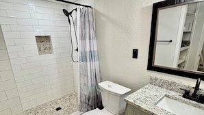 A bathroom with a shower, toilet, sink, and a mirror. - Casita Del Sol (Big Spring)