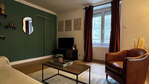 A living room with a sofa, a coffee table, a brown leather chair, a TV, and artwork on the walls.