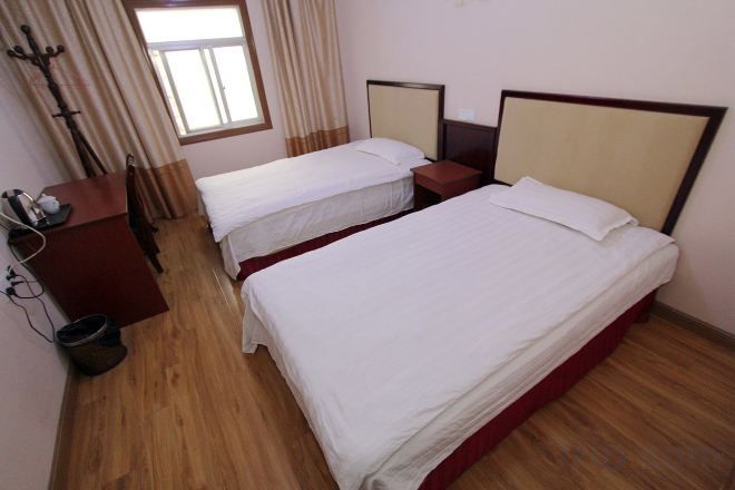 Habitación de hotel con dos camas individuales, piso de madera, escritorio con silla y ventana con cortinas.