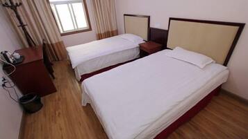 Habitación de hotel con dos camas individuales, piso de madera, escritorio con silla y ventana con cortinas.