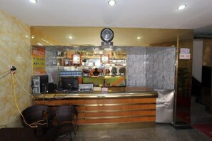 A reception area with a marble counter, a clock, and a computer. There are chairs and a small table with a plant. - Lianyungang Military Music Hotel (Lianyungang High-speed Railway Station Square Store) (Lianyungang)