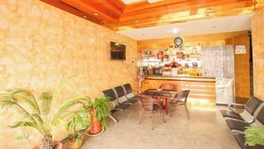 Un hall d’hôtel avec des poutres en bois au plafond, un comptoir d’accueil et plusieurs espaces aménagés avec des chaises et une petite table.