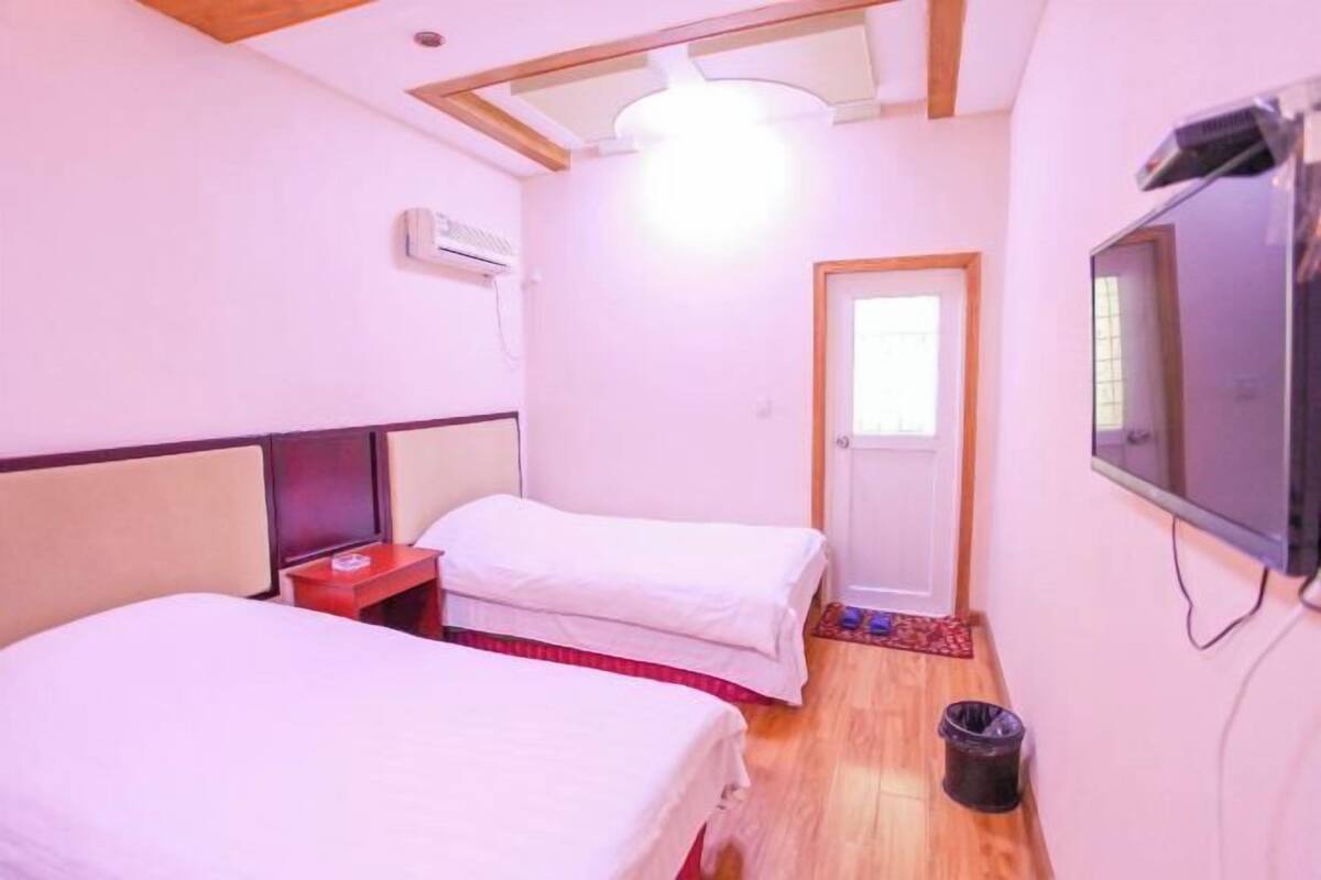 Une chambre avec deux lits, une télévision, un ventilateur de plafond et une porte.