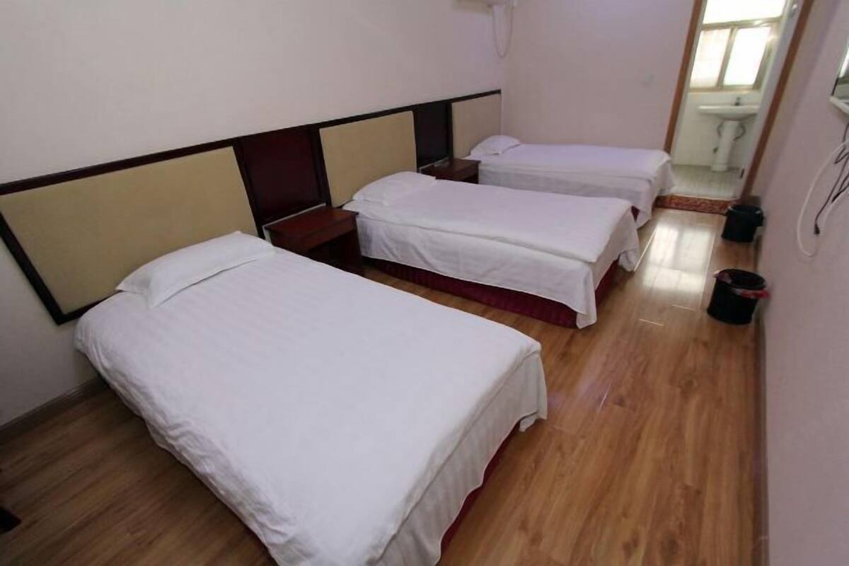 Une chambre d’hôtel avec deux lits simples, un plancher en bois, une petite table de chevet et une salle de bain visible au fond.