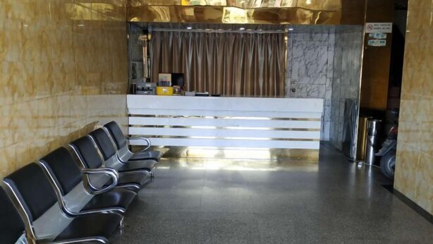 Un espace d’accueil avec un mur en marbre, un comptoir de réception et une rangée de chaises noires.
