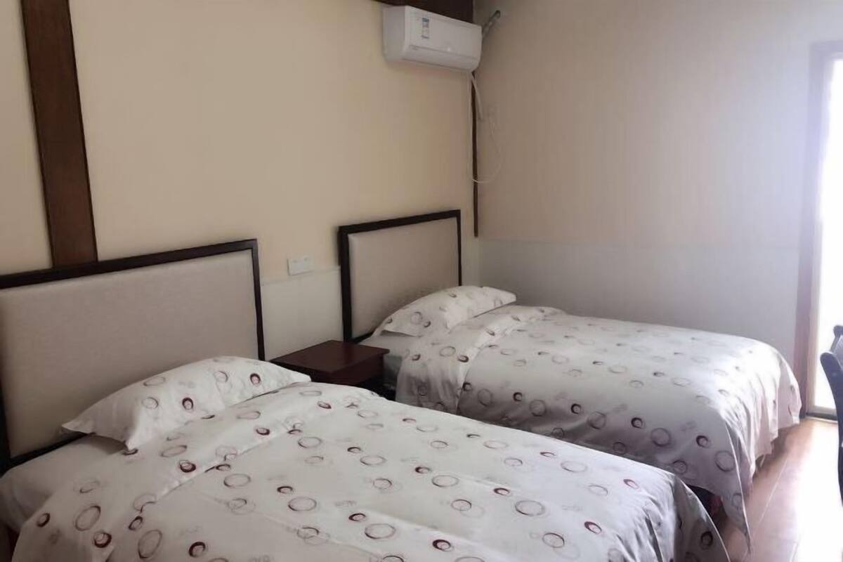 Une chambre dotée de deux lits, chacun avec une tête de lit, une table de chevet et un climatiseur fixé au mur.